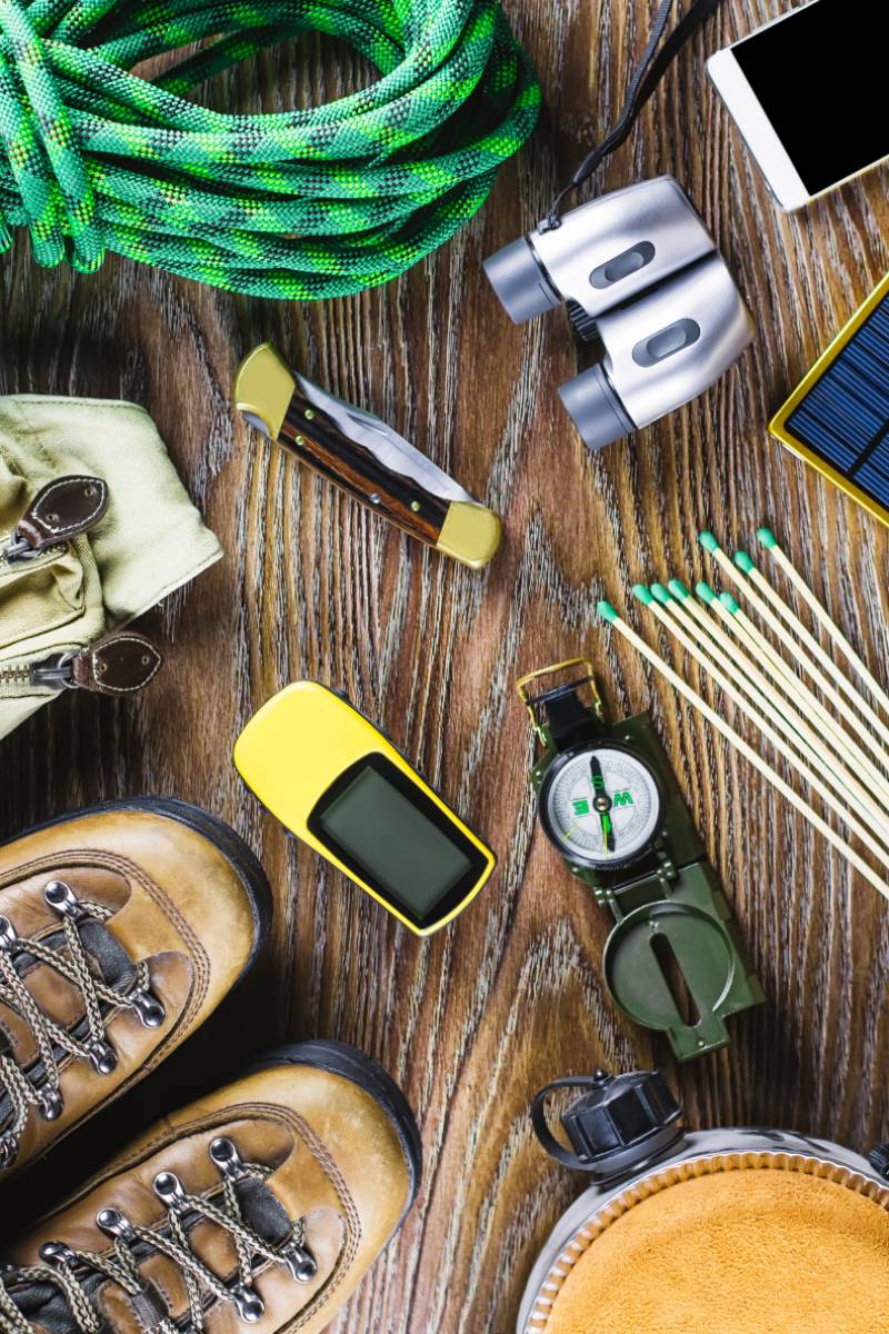 Hiking or travel equipment with boots, compass, binoculars, matches and travel bag on wooden background. Active lifestyle concept. Top view